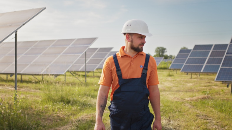 Industrial man engineer in uniform walking through solar panel field for examination. Ecological construction. Solar power station, Green energy concept. Solar station development and energy