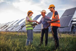 Ecological innovation and green energy concept at photovoltaic solar farm the ecological engineer old man and two his assistant discussing about the solar panels using the digital tablet
