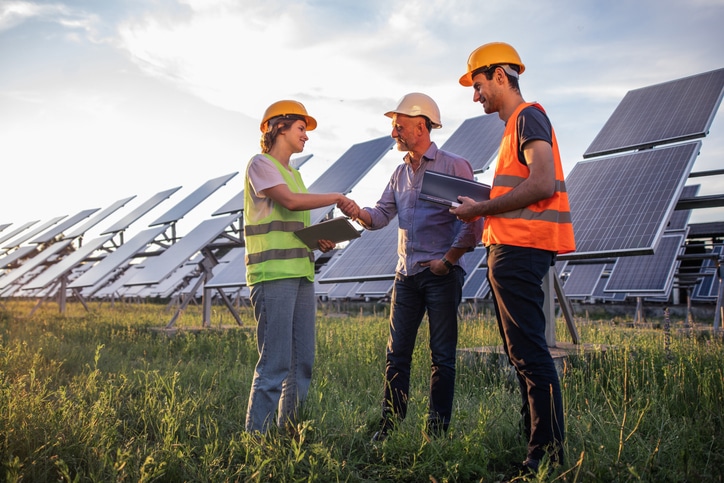 Ecological innovation and green energy concept at photovoltaic solar farm the ecological engineer old man and two his assistant discussing about the solar panels using the digital tablet