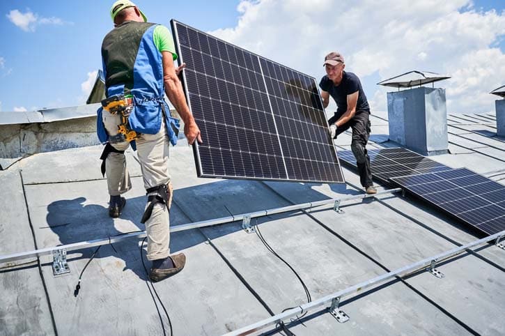 Workers building solar panel system on roof of house. Installers carrying photovoltaic solar module