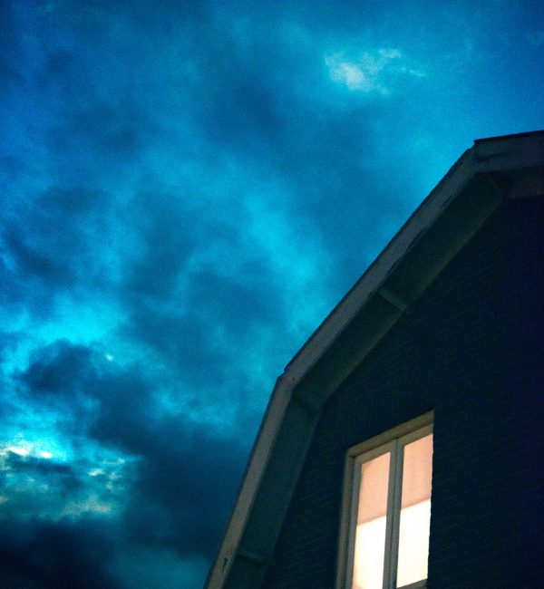 House with illuminated window under stormy sky.